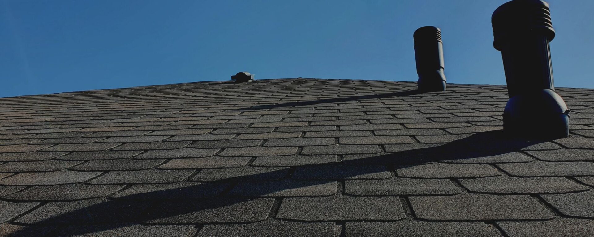 Asphalt shingle roof with two black chimneys against clear sky