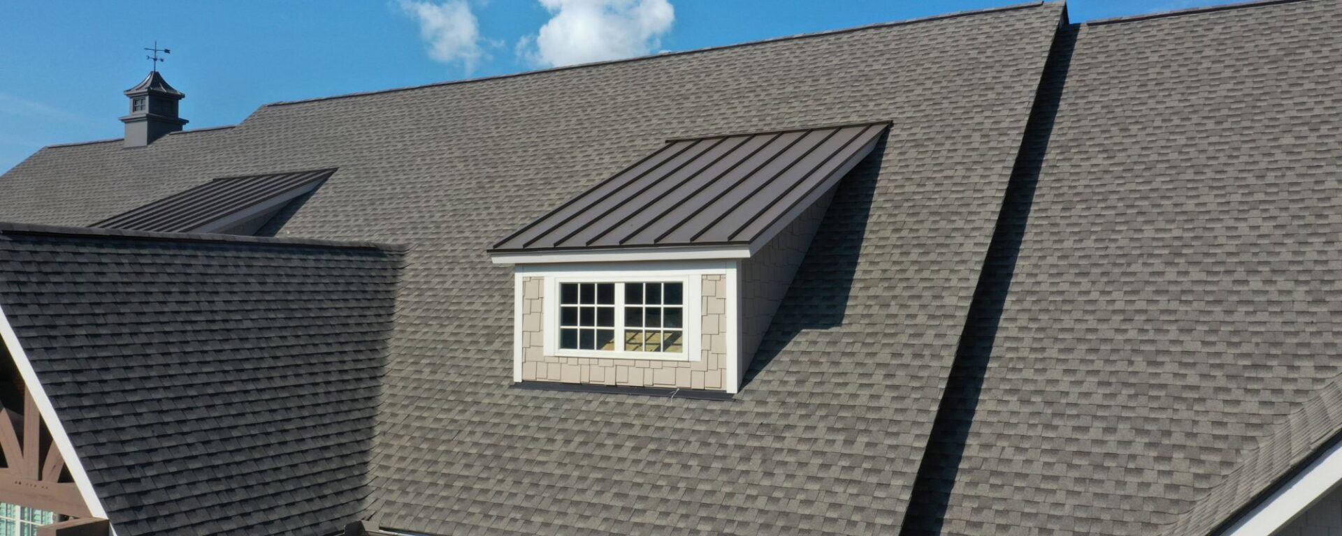 Gray asphalt shingle roof with white dormer window and metal roof accents