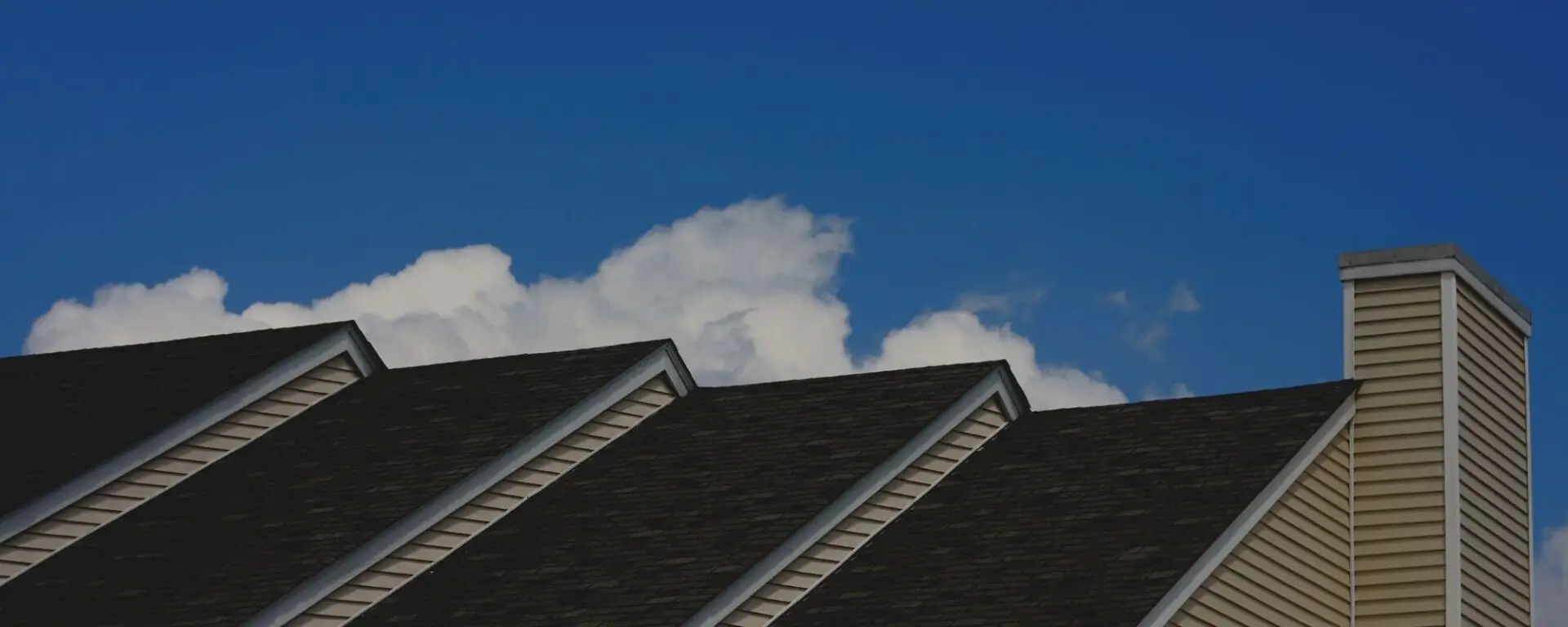 Residential roof with multiple gables and chimney against blue sky