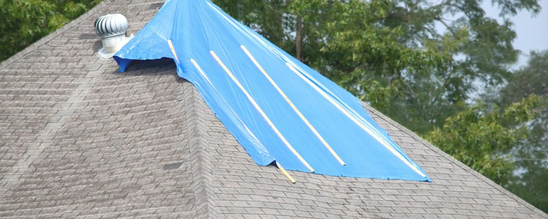 Blue tarp covering roof damage during emergency repair with exposed shingles