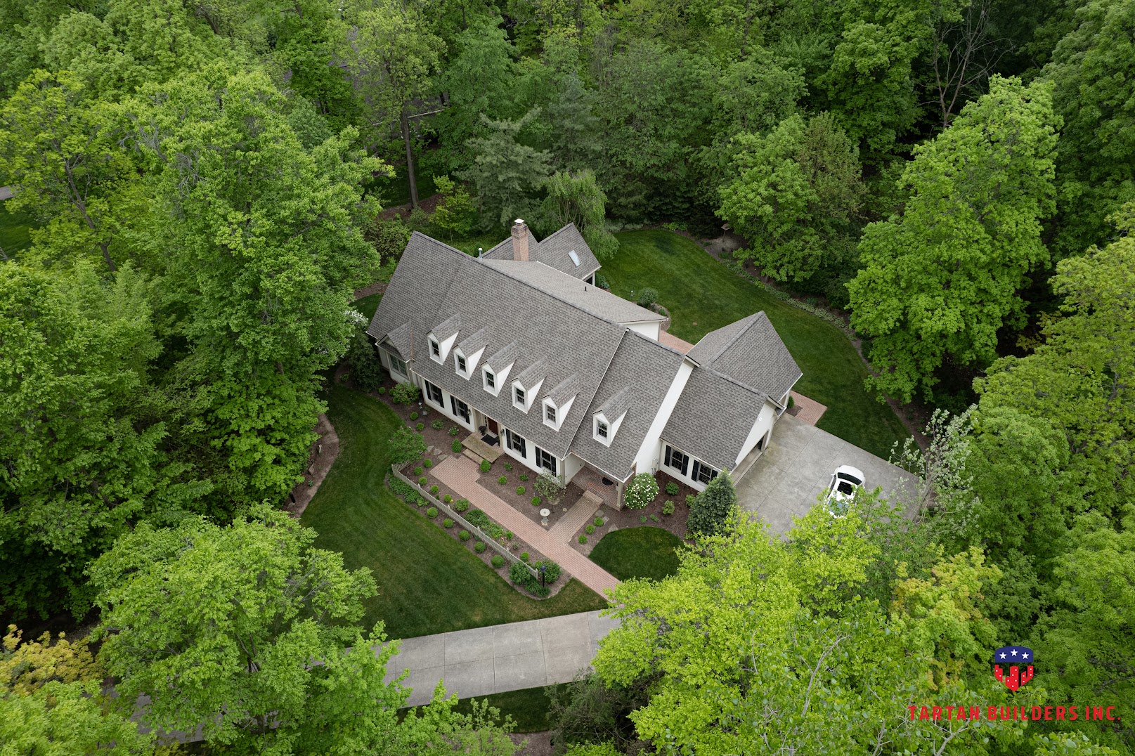 Aerial view of residential home with gray shingle roof surrounded by trees