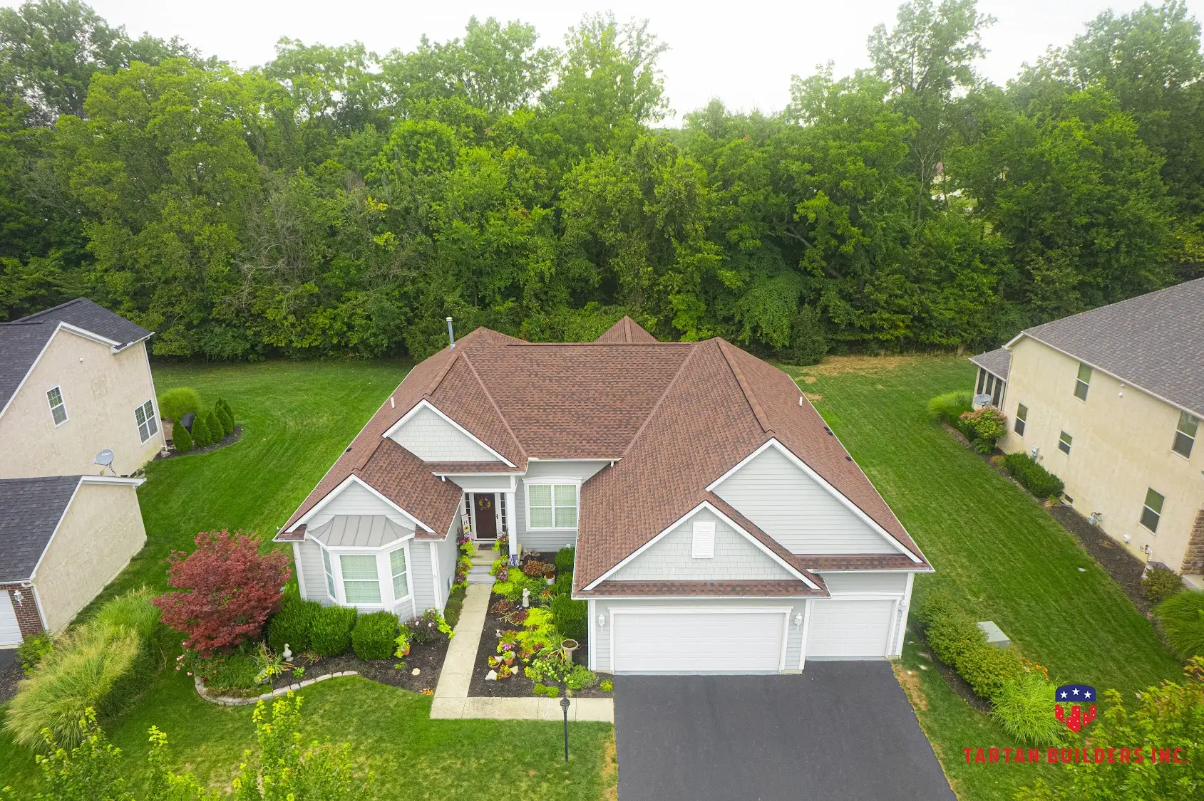 Aerial view of two-story brick home with brown architectural shingle roof and white siding