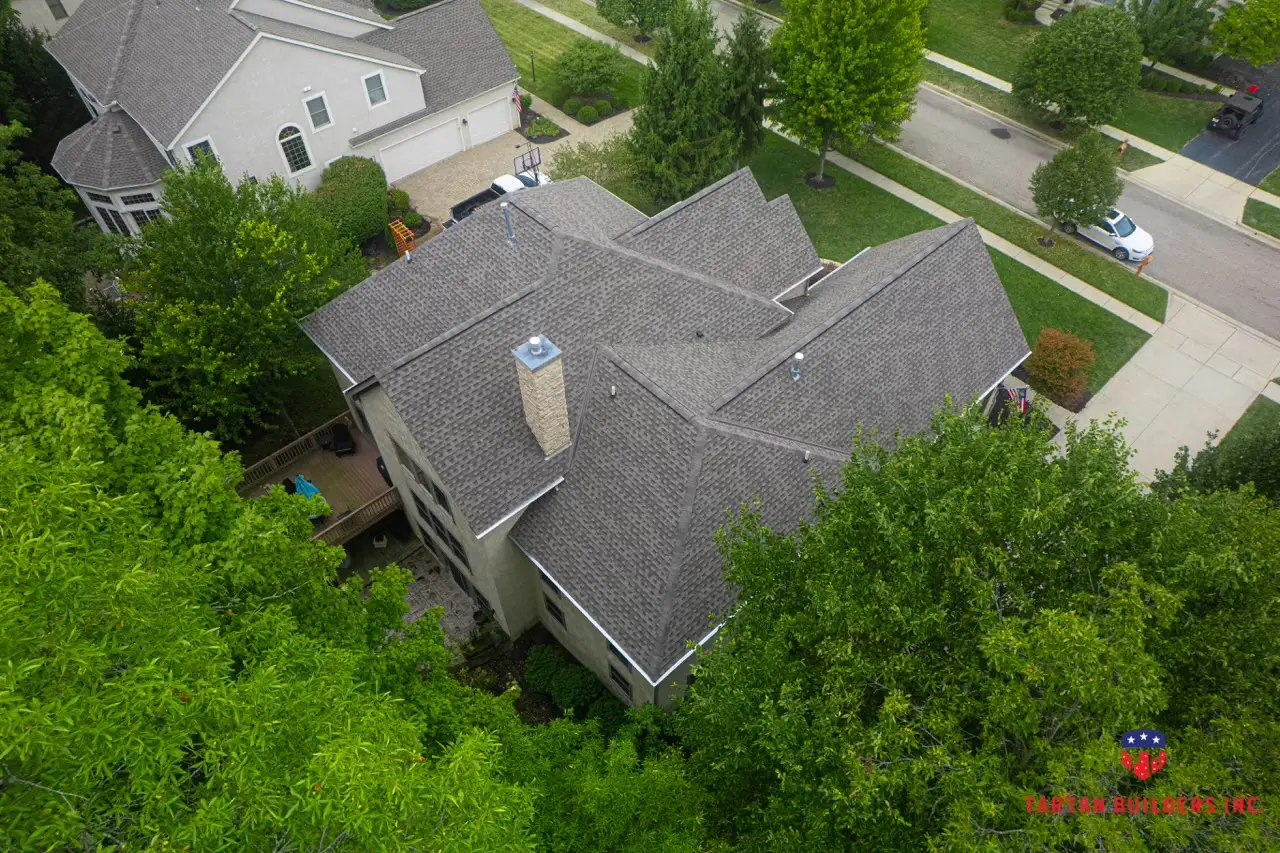 Aerial drone view of gray residential roof with stone chimney and complex architectural design