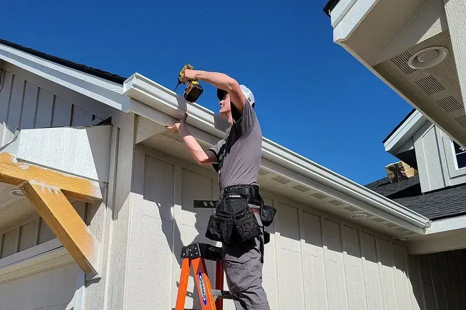 Professional installer securing seamless gutters on white residential home