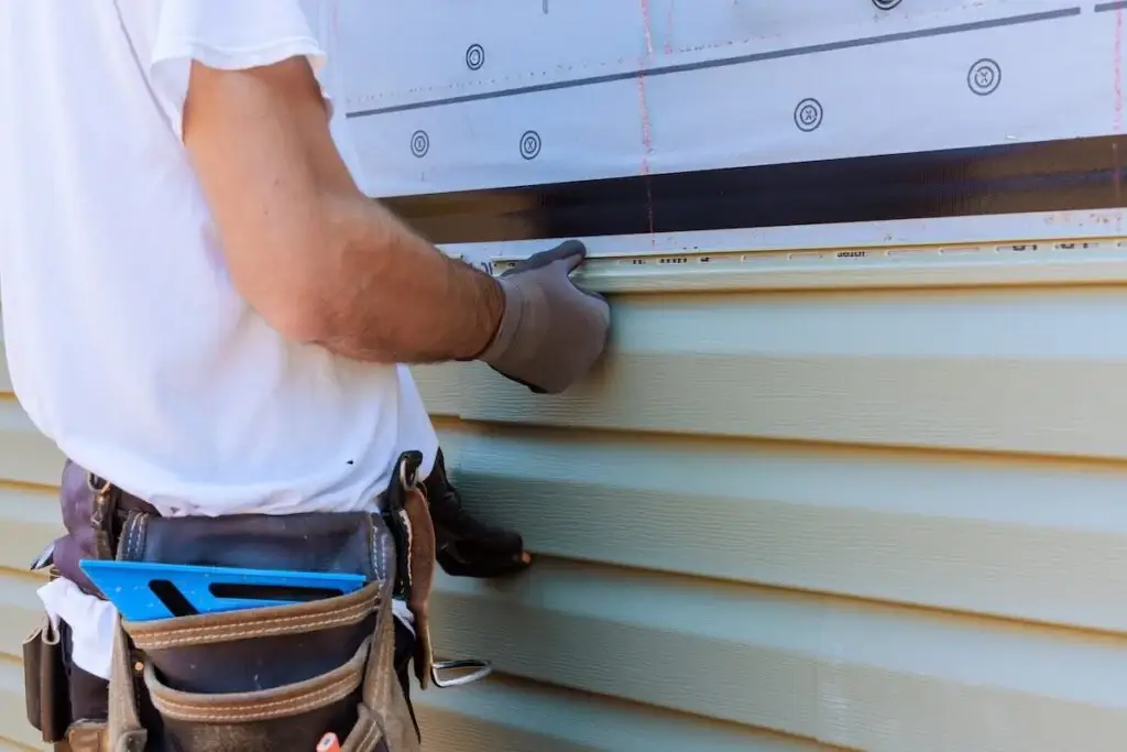 Contractor installing vinyl siding with a level and measuring tools